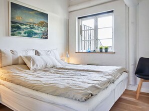A bedroom with a bed, a window, a chair, and a painting on the wall.