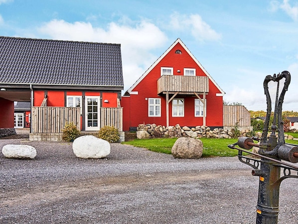 A red house with a grey roof, a wooden fence, and large rocks in the foreground.
