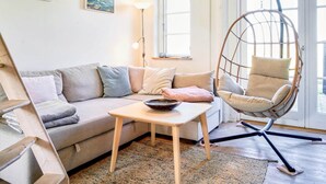 A cozy living room with a sofa, a hanging chair, a table with a bowl, and artwork on the walls.