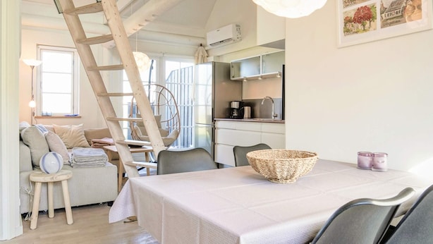 A cozy interior with a dining table, chairs, a wooden ladder, a hanging chair, and a kitchen area.