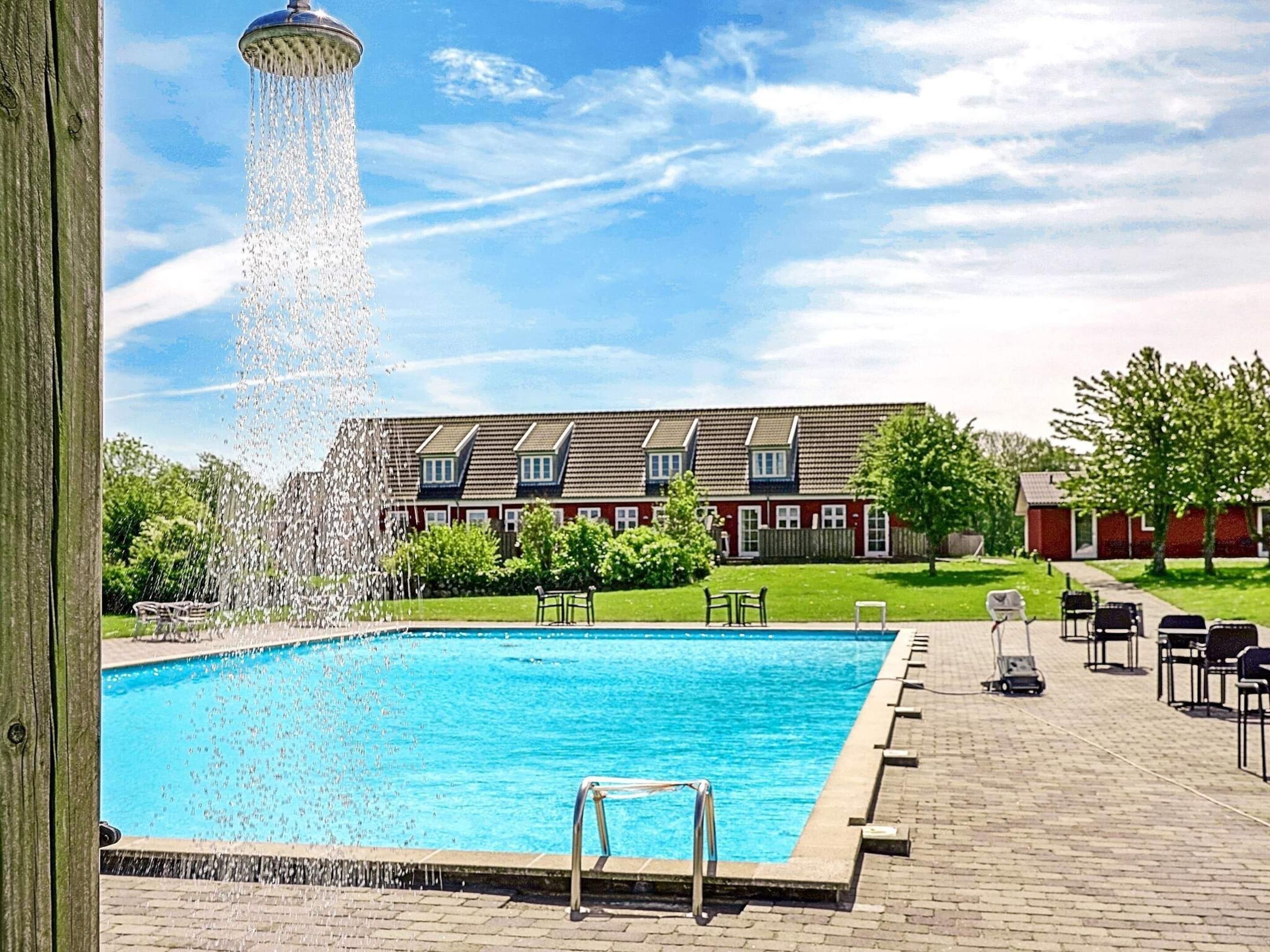 A swimming pool with a water fountain, surrounded by a brick deck and outdoor furniture.