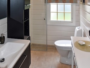 Een badkamer met een wit wastafelmeubel, een toilet en een raam boven het toilet.