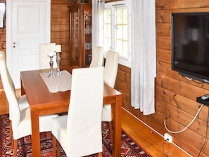 A wooden-paneled room with a dining table, chairs, a cabinet, a television, and a window with curtains. - Holiday Home in FrillesÃ¥s (Kristiansund)