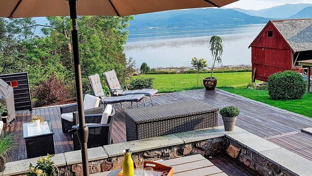 An outdoor patio with wicker furniture, a table with a tray of snacks, and a view of a lake and mountains.