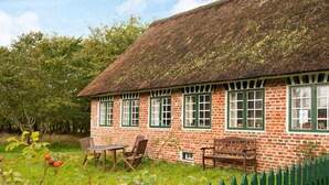 A traditional brick house with a thatched roof, green shutters, and a wooden fence. - 6 Person Holiday Home in Fano (Fano)