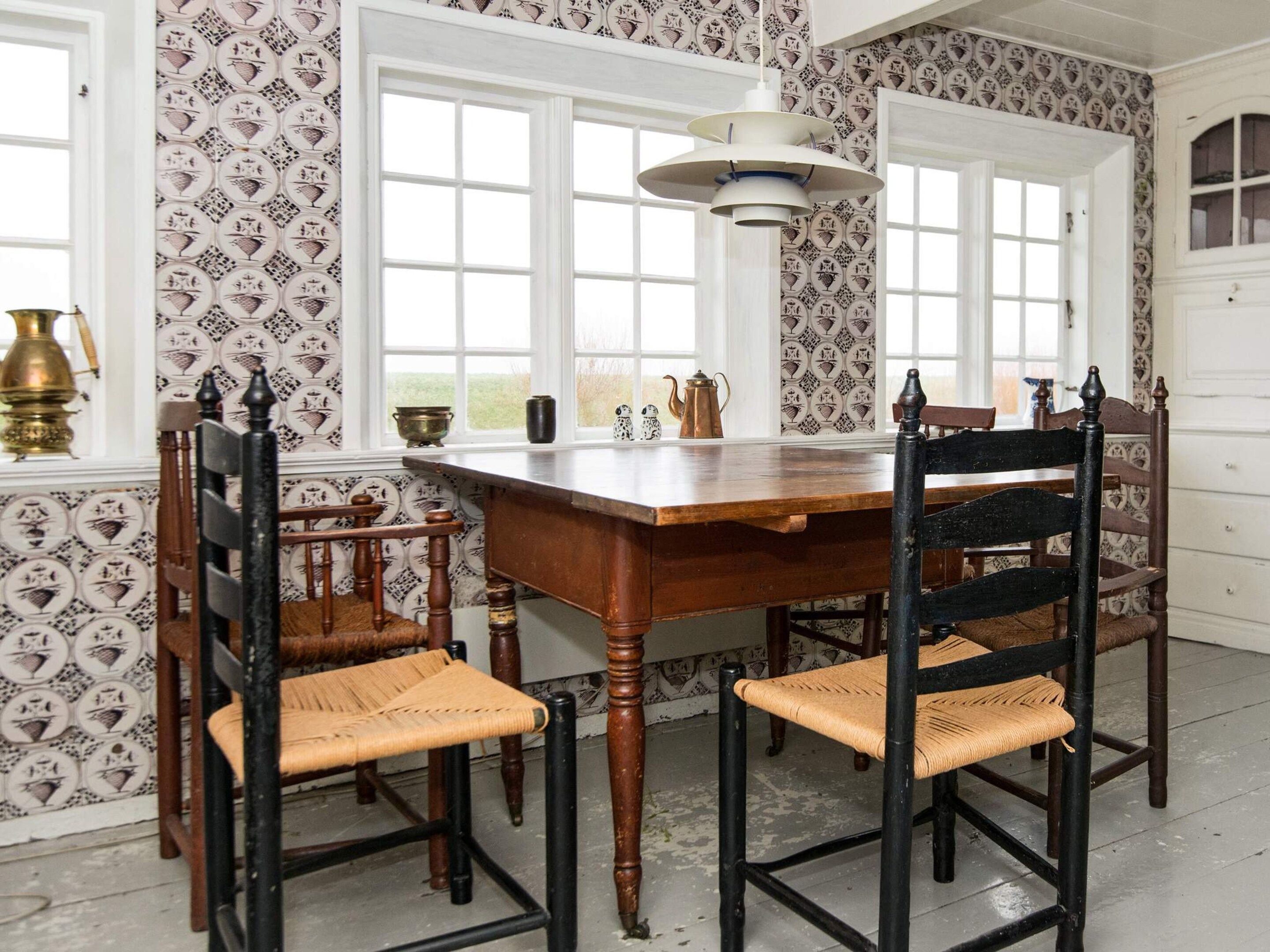 A dining area with a wooden table and chairs, patterned wallpaper, and a window with a view.