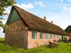 A traditional brick building with a thatched roof, a green door, and a small table with chairs in the foreground. - 6 Person Holiday Home in Fano (Fano)