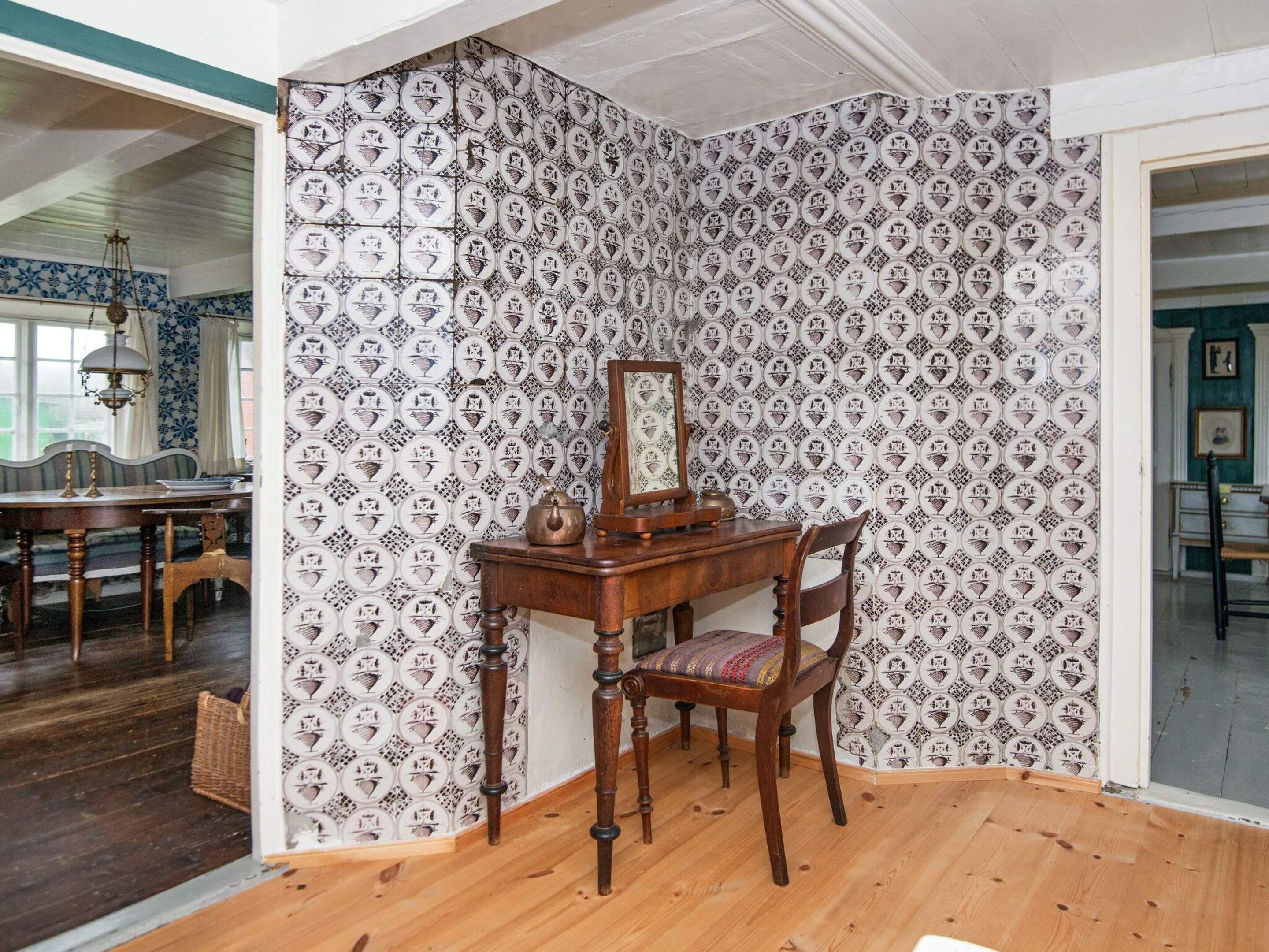 A room with a patterned wallpaper, a wooden desk with a mirror, and a chair.