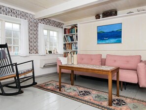 A living room with a rocking chair, a pink sofa, a wooden coffee table, a bookshelf, and a painting of a seascape. - 6 Person Holiday Home in Fano (Fano)