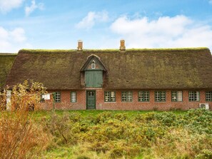 A traditional brick house with a thatched roof, a central chimney, and a green door. - 6 Person Holiday Home in Fano (Fano)