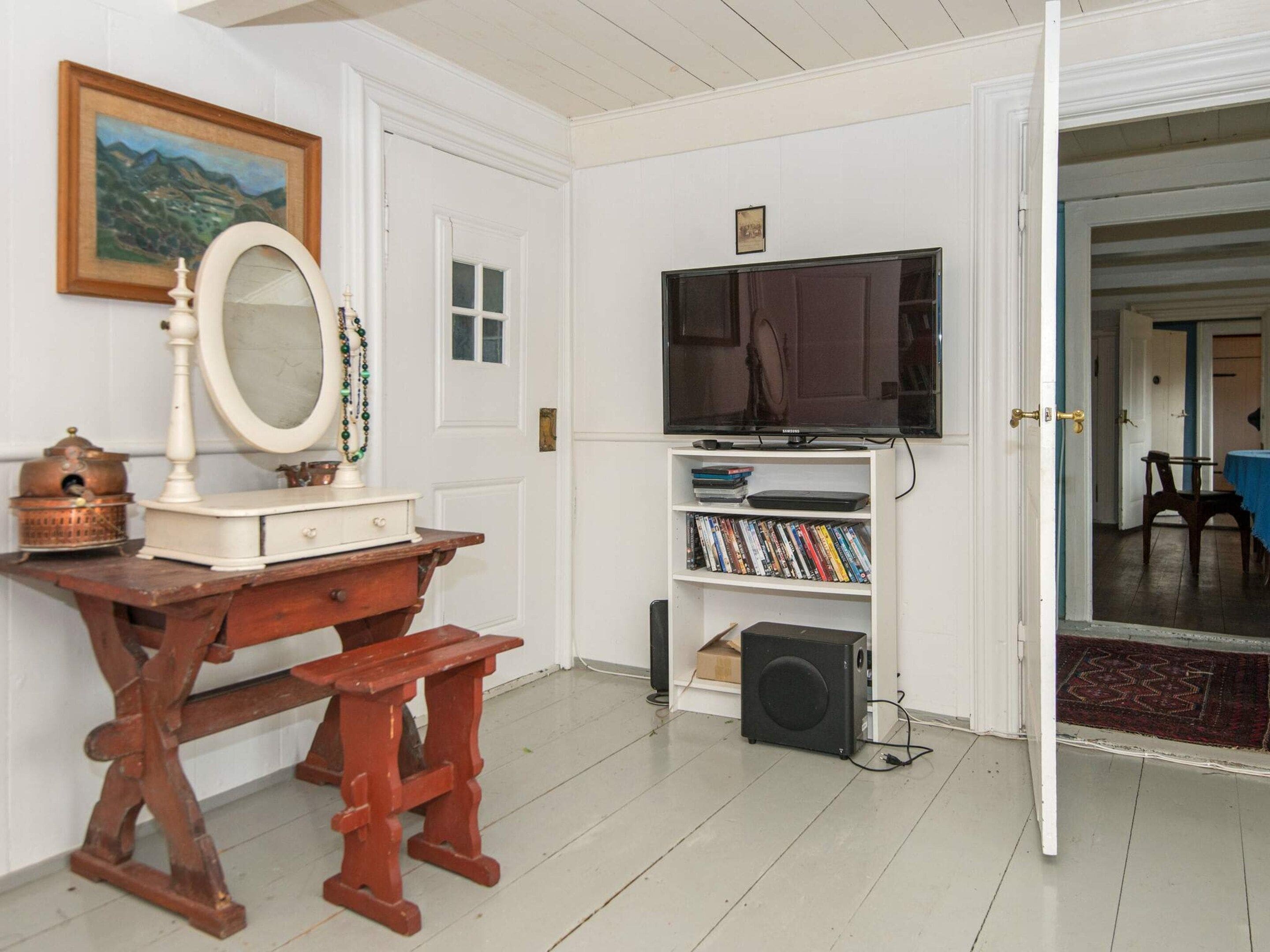 Een kamer met een houten bureau, een spiegel, een televisie op een standaard en een boekenkast met dvd's.