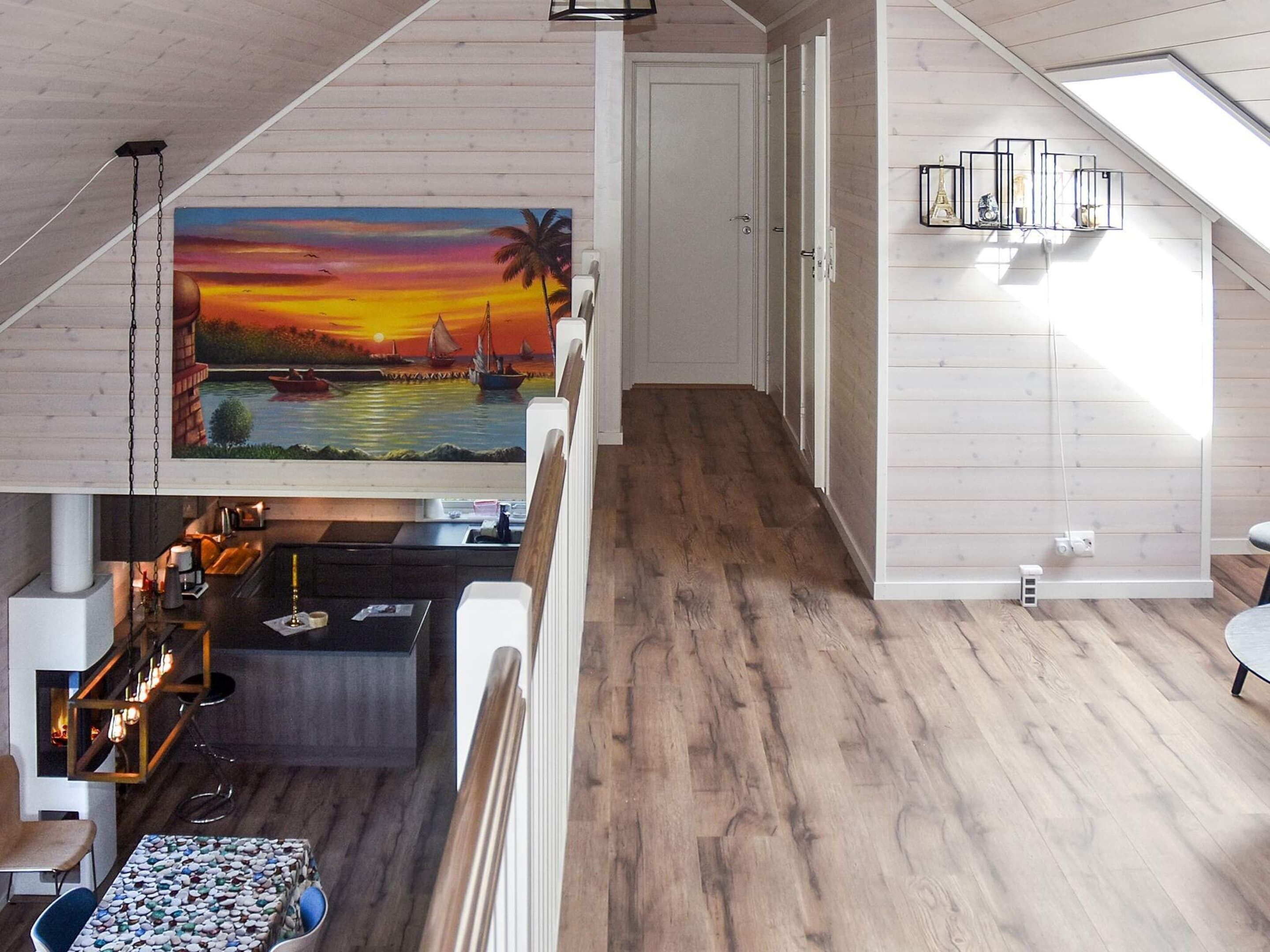 A modern interior with a wooden floor, a painting of a sunset over water, a bar area, and a staircase leading to another level.