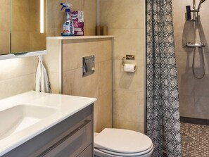 Een badkamer met een wit wastafel, toilet, douche met een decoratieve gordijn en een Persil Universal fles op een plank.