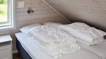 A bedroom with a sloped ceiling, a bed with white bedding, a bedside table, and a window with a view of greenery.