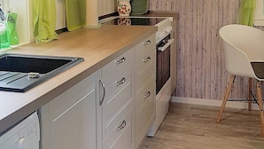 Una cocina con encimera de madera, un lavamanos y lavavajillas. Hay una silla y un jarrón con flores en la encimera.