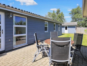 A patio area with a table and chairs, a small garden, and a house with a blue exterior.