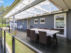 A covered outdoor patio with a table and chairs, a small garden area, and a house with a door and windows.