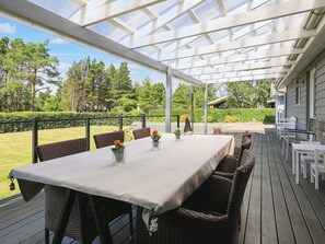 An outdoor patio with a covered dining area, wicker furniture, and a view of the surrounding greenery.