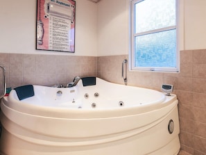 A bathroom with a large bathtub, a window, and a poster on the wall.