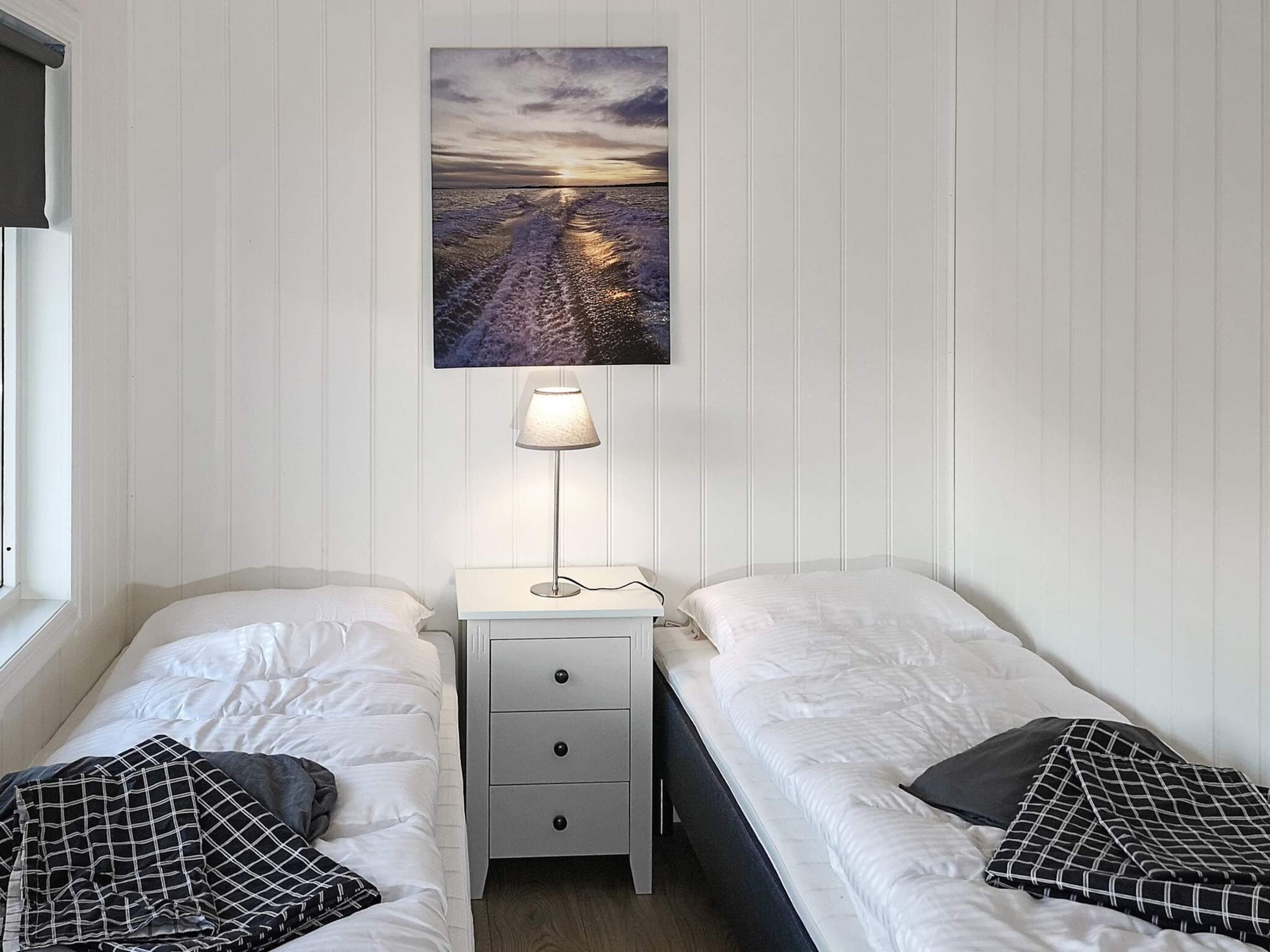 A twin room with two beds, a nightstand with a lamp, a wall-mounted painting, and a window.