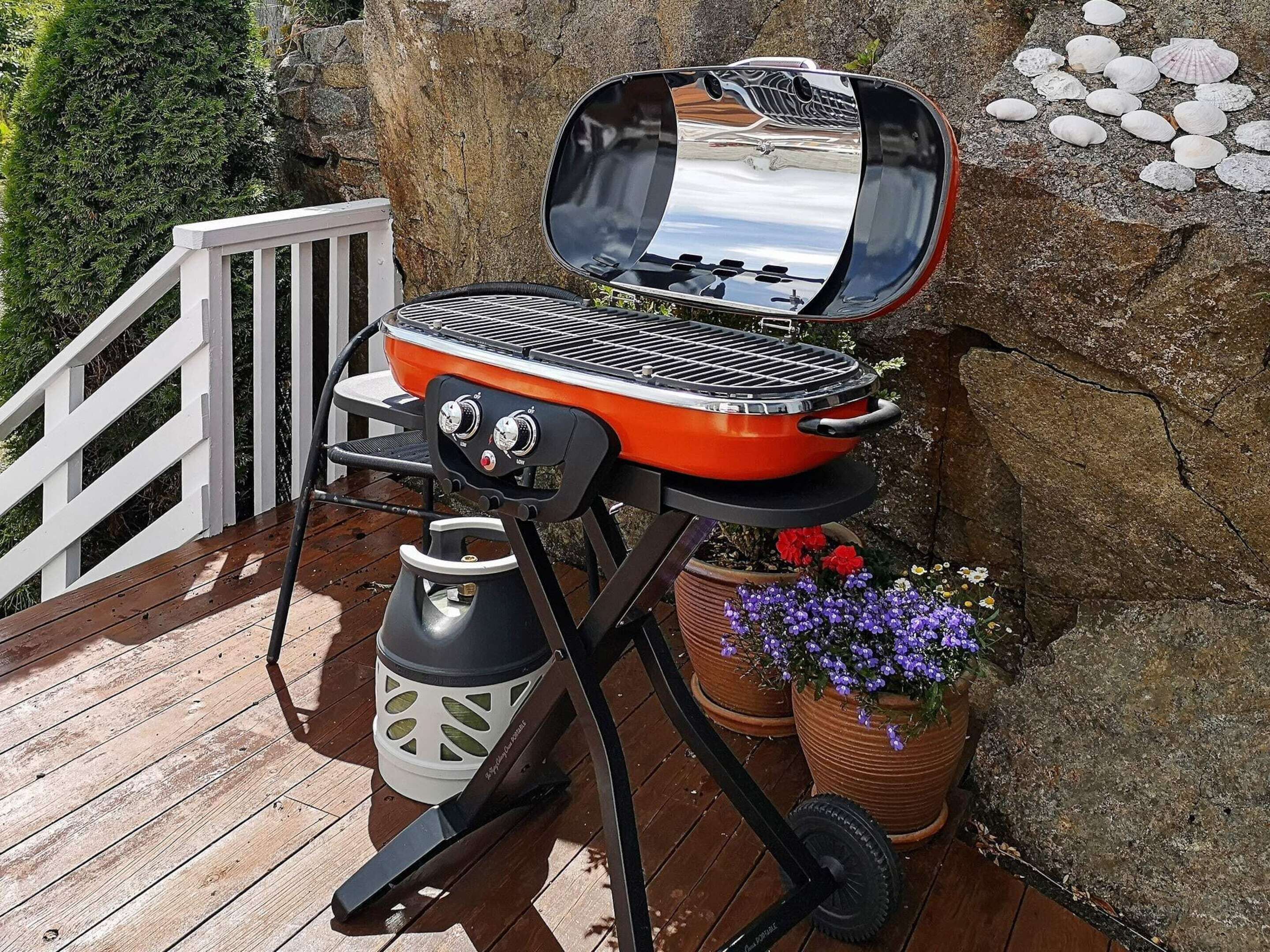 Ein tragbarer Grill auf einer Holzdielen Terrasse mit einer Steinmauer und Topfpflanzen.