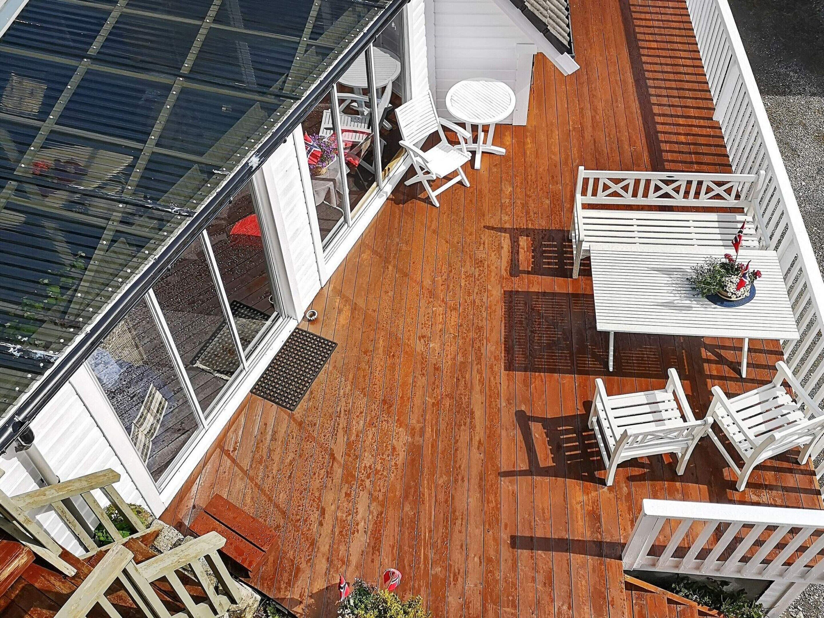 An outdoor deck with a wooden floor, white furniture, and a glass enclosure.