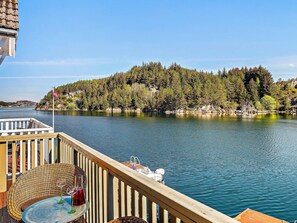 Une vue sur le lac, avec une terrasse en bois, une table sur laquelle se trouvent une bouteille et un verre, et une maison située sur une colline.