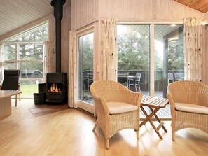 A cozy room with a fireplace, wicker chairs, a table, and large windows offering a view of the outdoors.