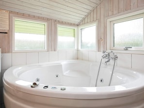 A large, white, freestanding bathtub in a room with wooden paneling and three windows with frosted glass.