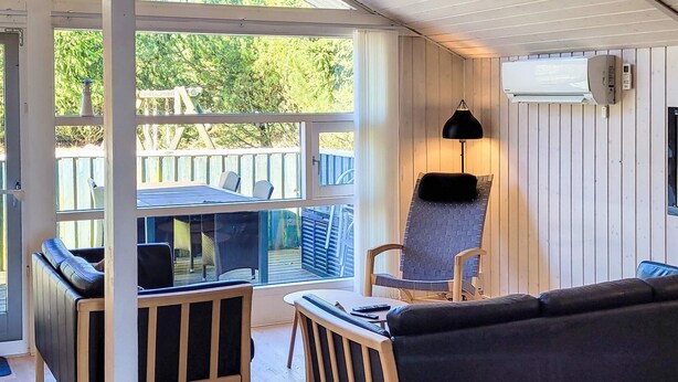 A covered outdoor seating area with a table and chairs, a cushioned bench, and a lamp. - 6 Person Holiday Home in Lokken (Lokken)