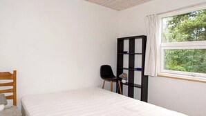 A small, neatly arranged bedroom with a single bed, a wooden chair, a black shelving unit, and a window with a view of greenery. - 6 Person Holiday Home in Skjern (Skjern)