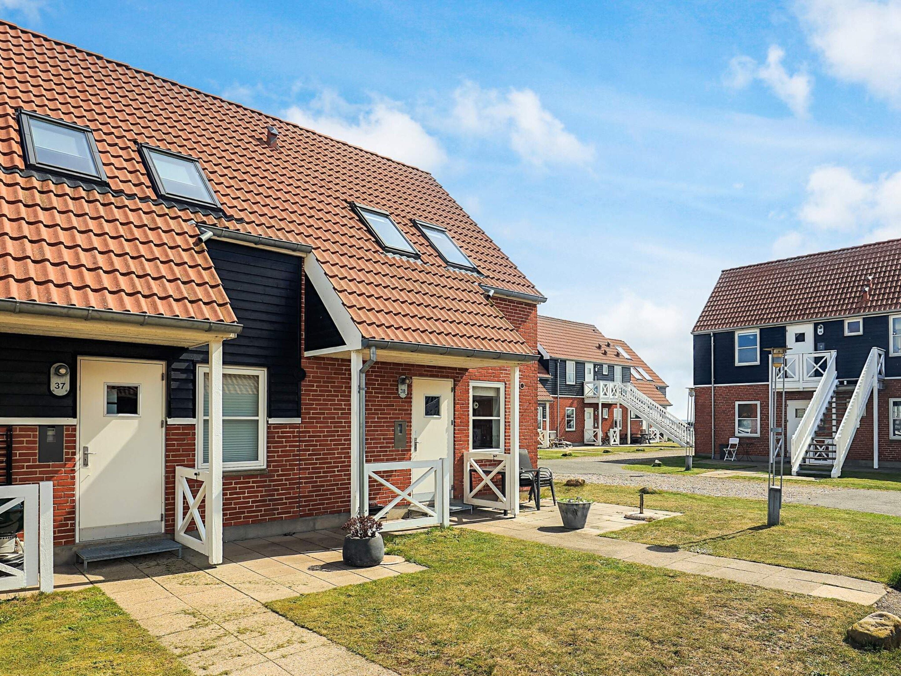 Une rangée de maisons de ville avec des toits recouverts de tuiles rouges, des façades en briques et de petits jardins devant.