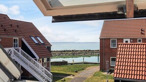 A view of a coastal property with a paved pathway leading to a dock, a small building with a red-tiled roof, and a staircase leading to a balcony. - 4 Person Holiday Home in Borre (Borre)