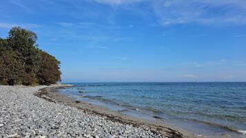 Une plage de galets, avec un ciel dégagé et une mer calme.