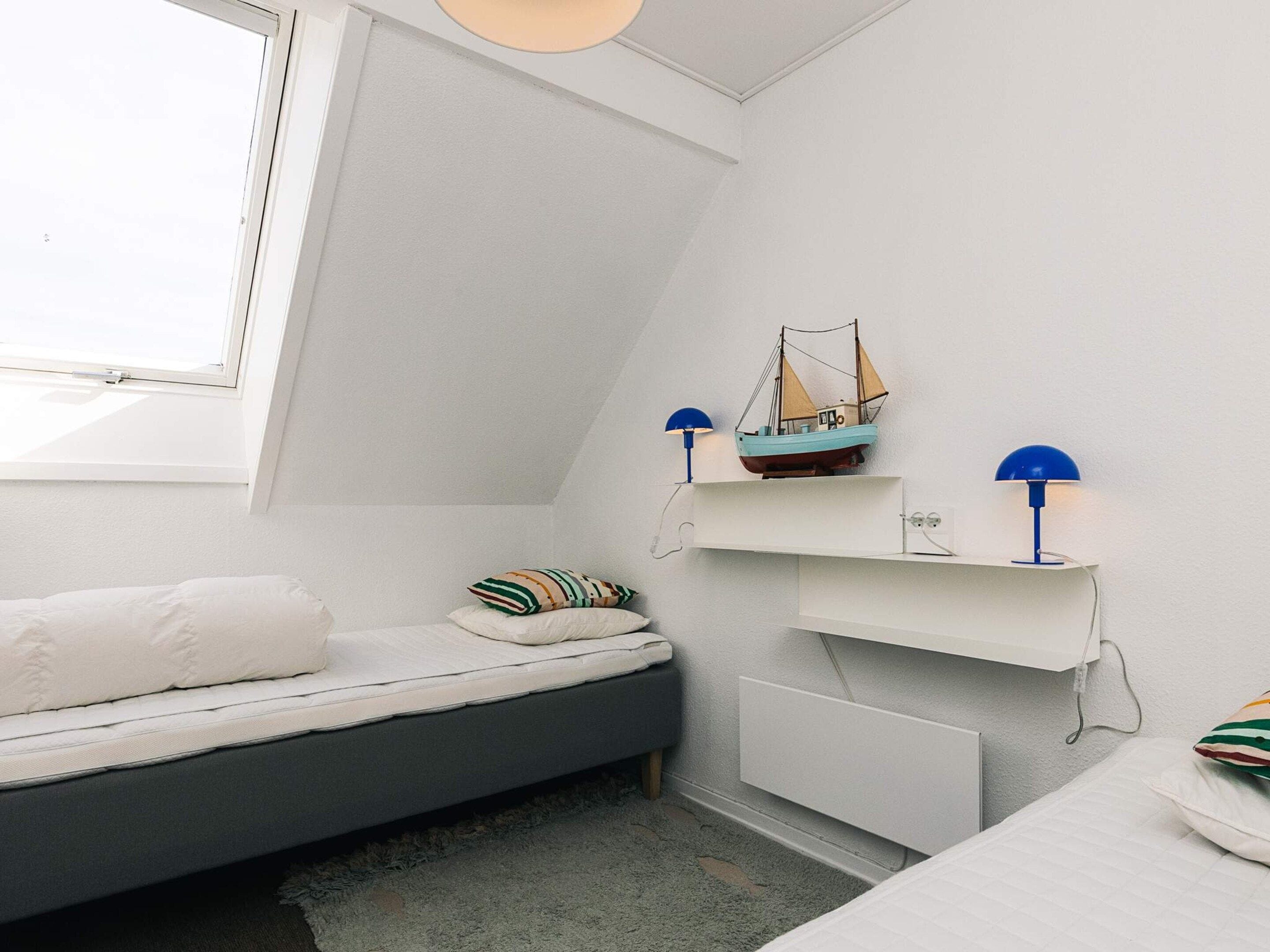 Cama litera infantil con un pequeño estante arriba, una ventana y un modelo de barco en el estante.