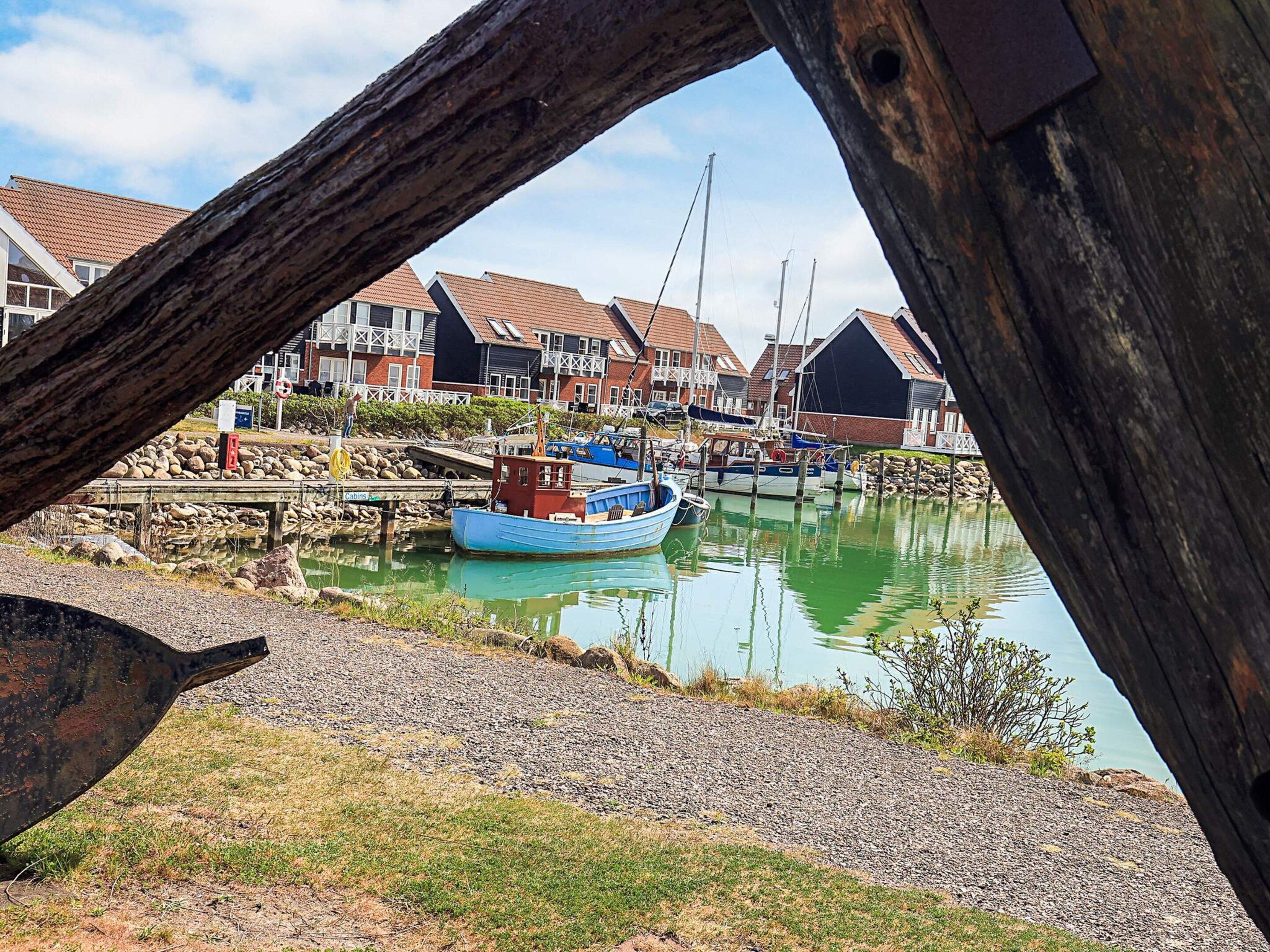 Un port où sont amarrés des bateaux, une jetée en bois et des maisons en arrière-plan.