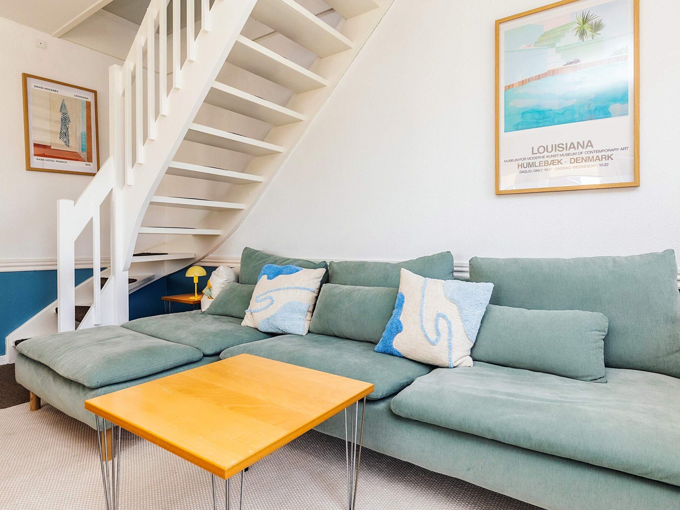 Un salon moderne avec un canapé vert, une table basse en bois et un escalier blanc.