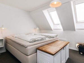A loft bedroom with a sloped ceiling, a bed with a beige mattress and white bedding, a wooden bench at the foot of the bed, and a skylight. - 4 Person Holiday Home in Borre (Borre)