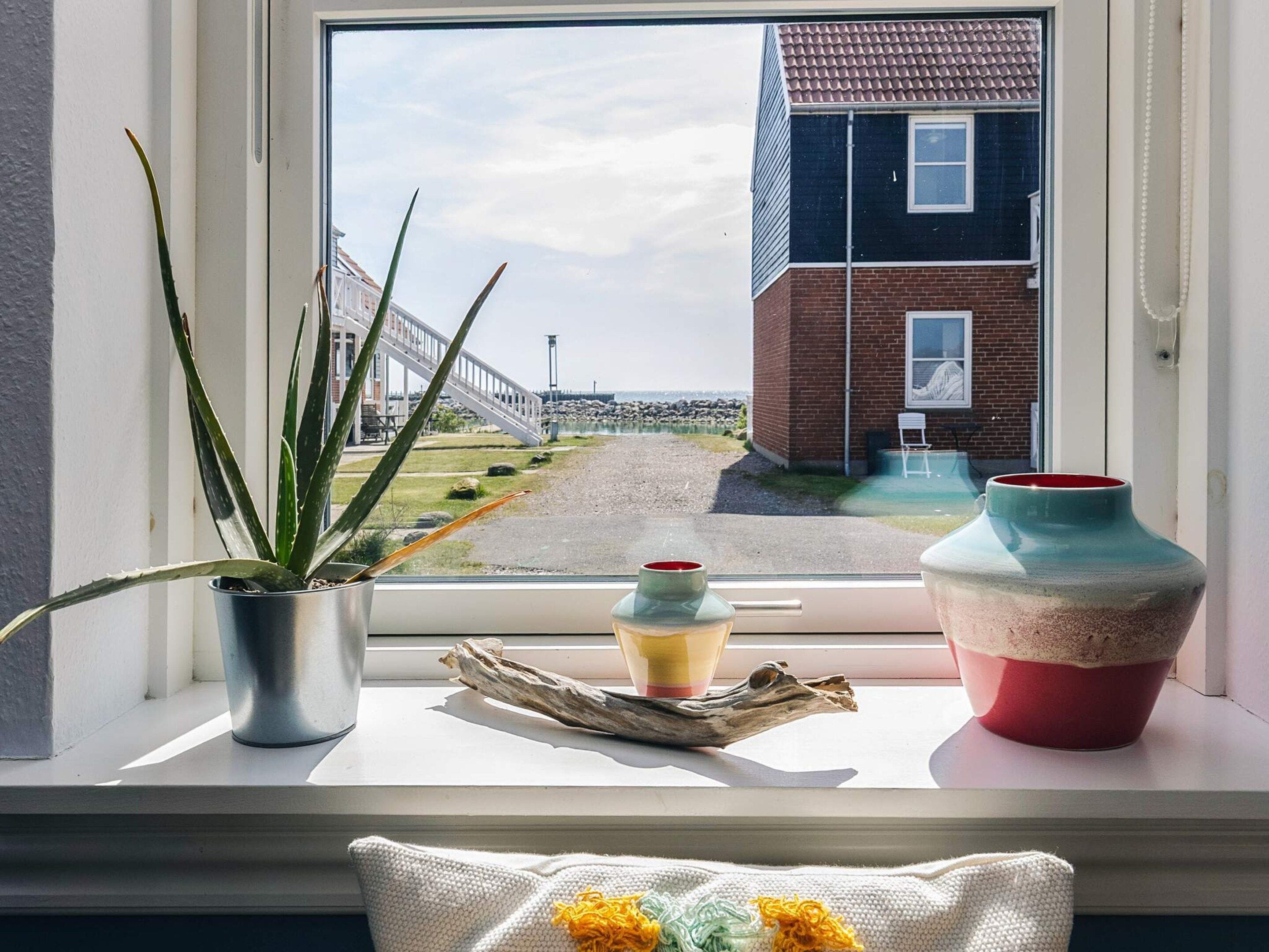 A window with a view of a brick building, a metal pot with a plant, and two ceramic vases on a windowsill.