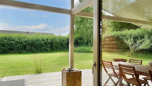Une terrasse en bois avec une porte vitrée donnant sur un jardin.