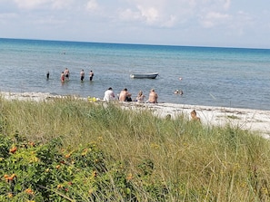 A beach with people swimming and a boat in the water. - 4 Star Holiday Home in Glesborg (Glesborg)