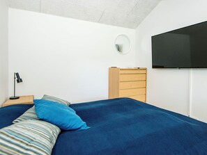 A bedroom with a bed, a dresser, a round mirror, and a flat-screen TV mounted on the wall. - 4 Star Holiday Home in Glesborg (Glesborg)