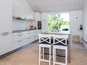A modern kitchen with white cabinets, a built-in oven, a coffee maker, and a large window offering a view of greenery. - 4 Star Holiday Home in Glesborg (Glesborg)