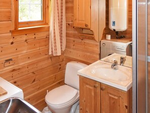 Une petite salle de bain en bois, aménagée dans une cabane, avec des toilettes, un lavabo et une fenêtre dotée d’un rideau.