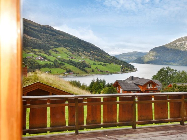 Une terrasse en bois donnant sur un lac, avec des maisons et des collines en arrière-plan.