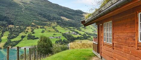 A wooden cabin with a view of a green valley and mountains.