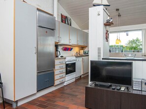 A modern kitchen with a refrigerator, stove, oven, microwave, and a flat-screen TV on a wooden cabinet. - 4 Person Holiday Home in Aabenraa (Aabenraa)