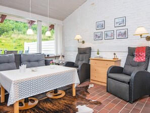 A cozy room with a white brick wall, a dining table with chairs, and a sofa. There are wall-mounted lamps and framed pictures on the wall. - 4 Person Holiday Home in Aabenraa (Aabenraa)