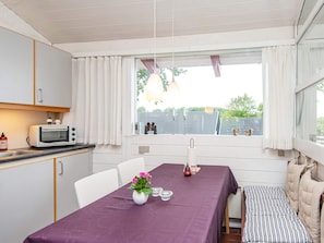 A compact kitchen with a microwave, a dining table with a purple tablecloth, and a window with curtains.