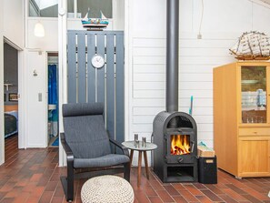 Ett mysigt rum med en vedeldad kamin, en bekväm fåtölj, ett litet bord och ett skåp med glasdörrar.